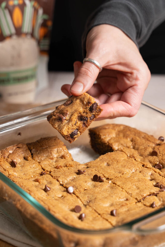 Hand pulling a brown butter blondie out of the pan