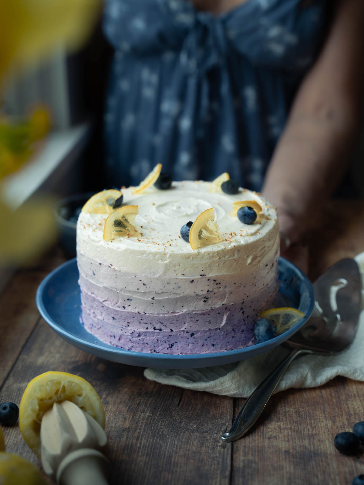Woman placing a lemon blueberry cake onto a serving table
