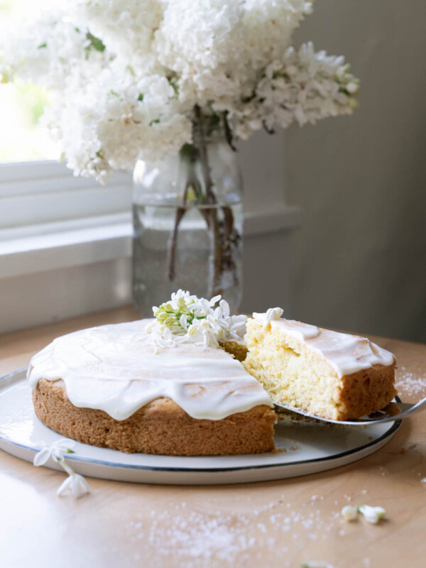 A lemon and lilac cake in front of a vase of fresh lilac flowers