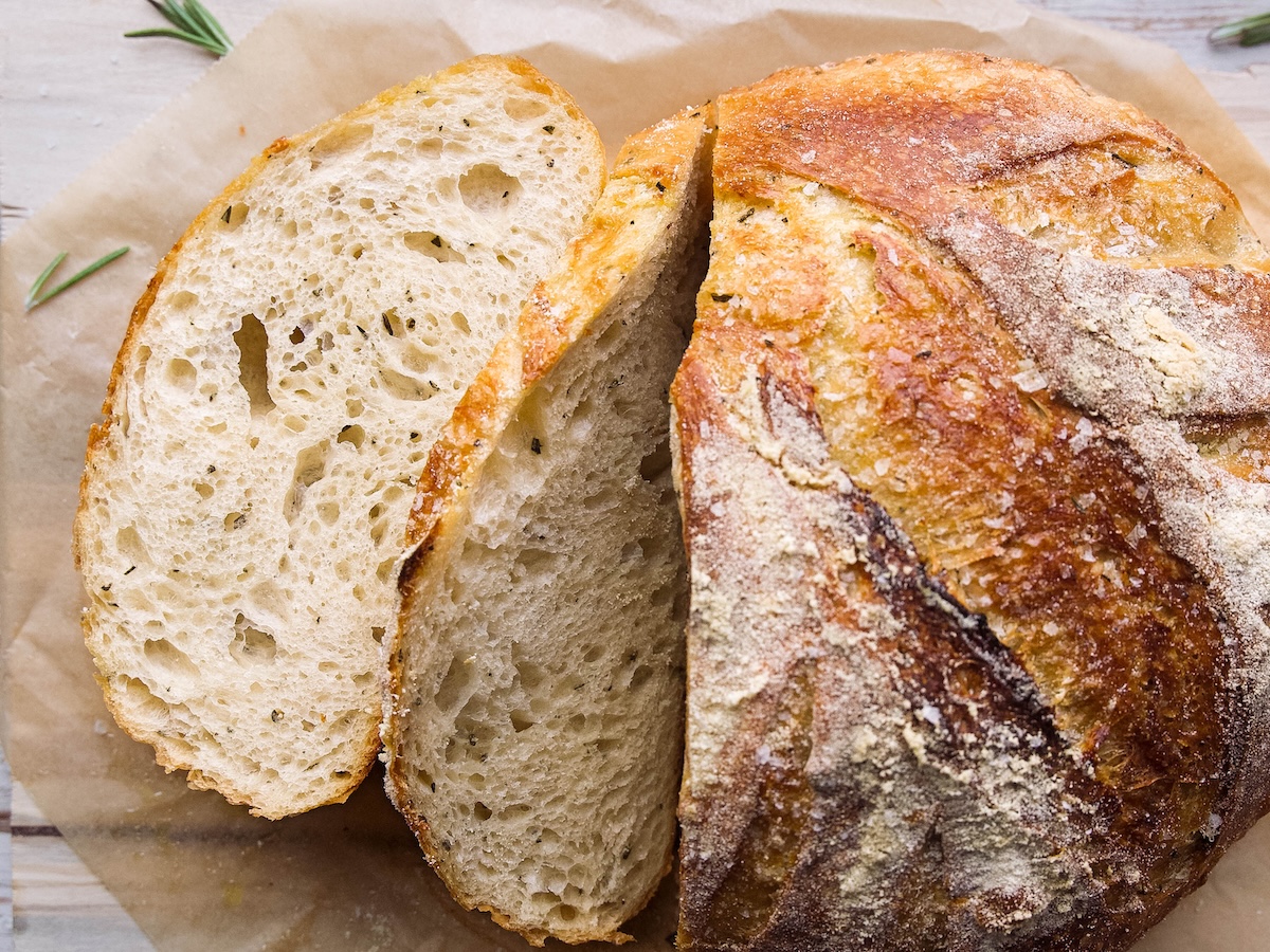 A loaf of rosemary sourdough bread with a few slices cut into it