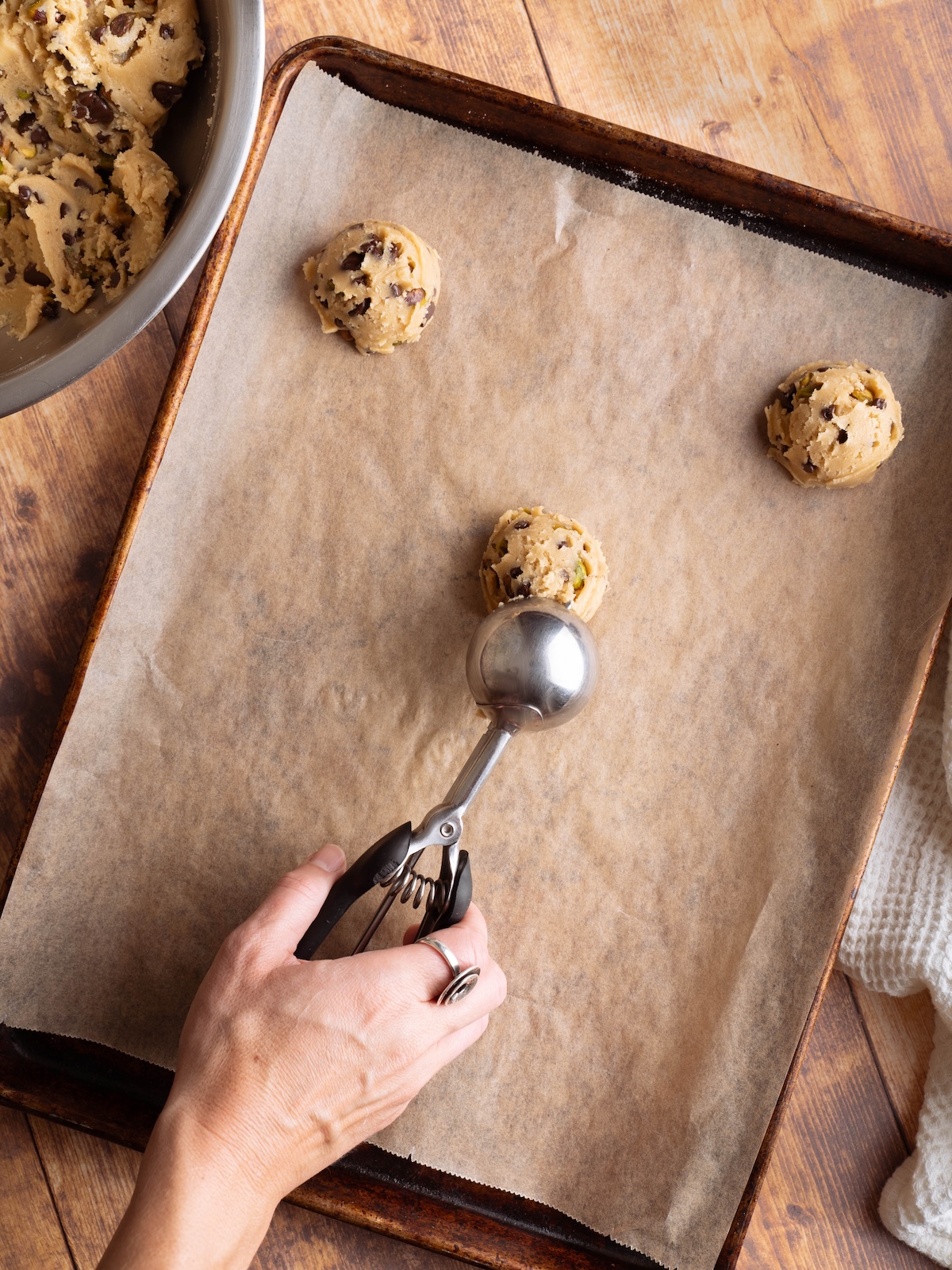 Scooping pistachio chocolate chip cookie dough onto a baking sheet