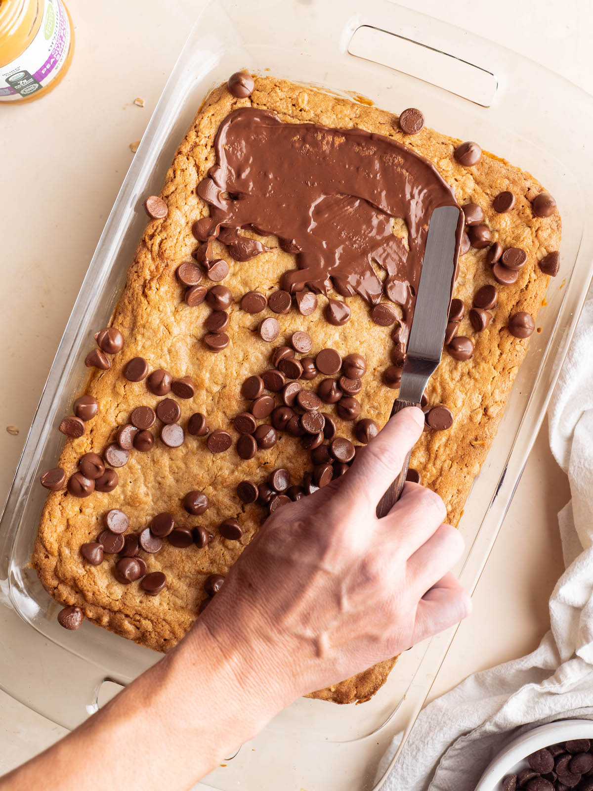Spreading melted chocolate chips onto peanut butter cookie bars