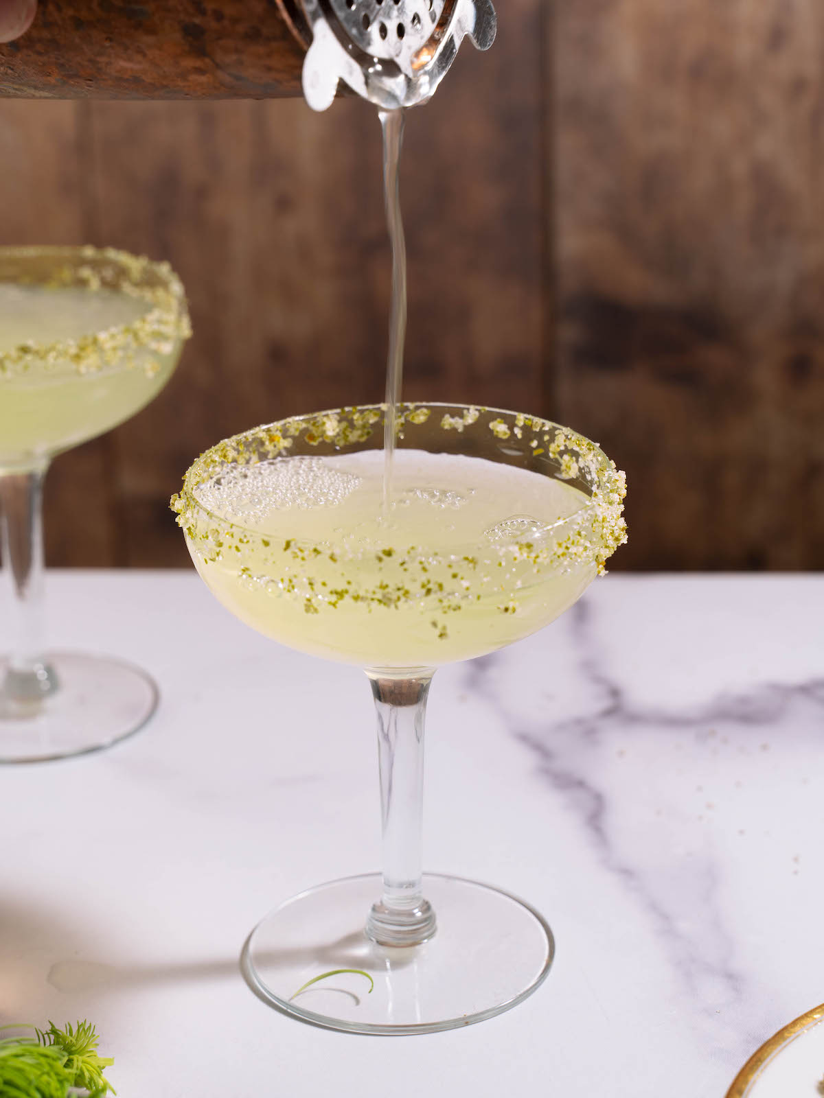 Pouring fir tip lemon drop cocktail mixture into a coupe glass