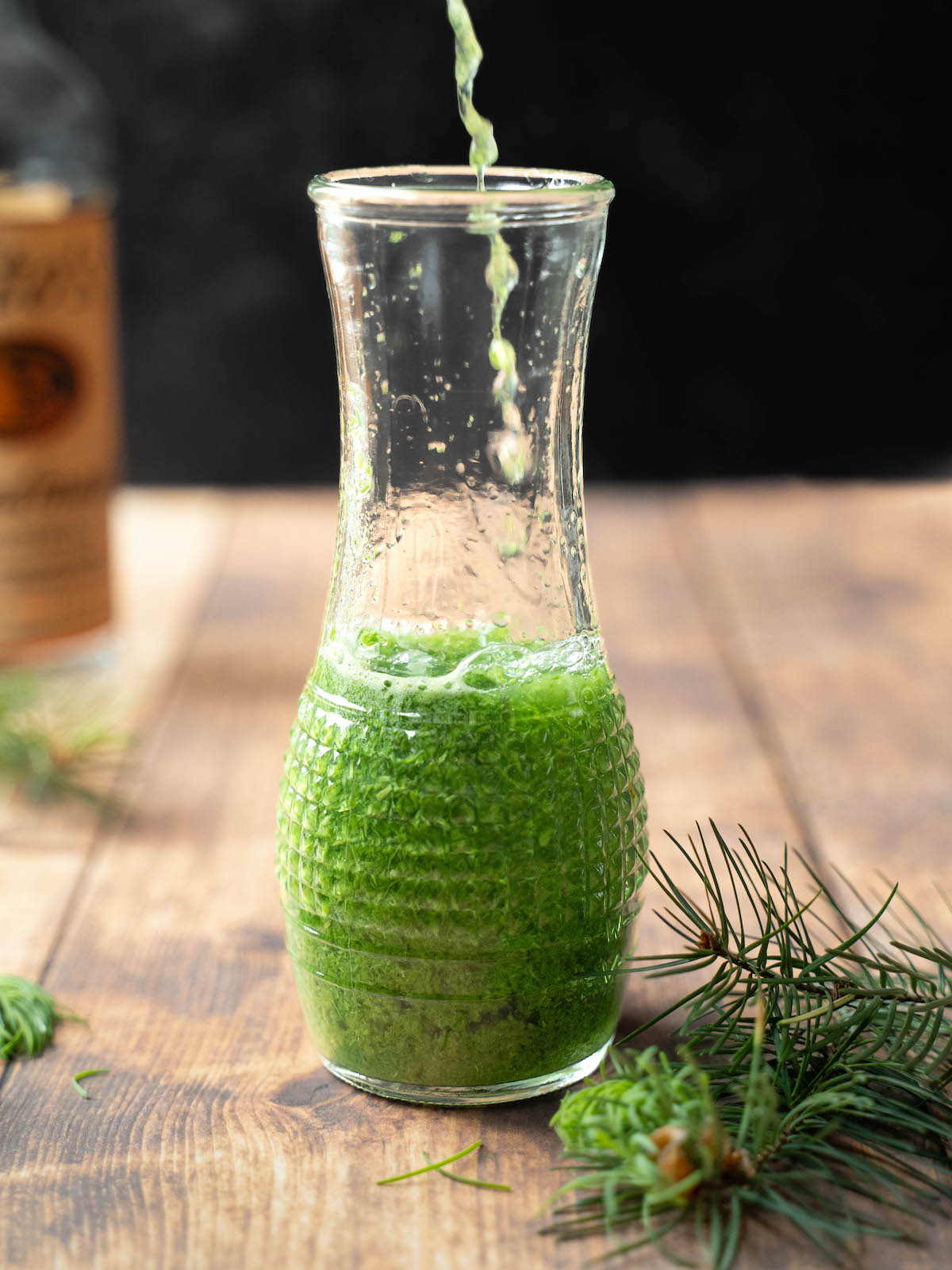 Fir tip-infused vodka pouring into a glass jar