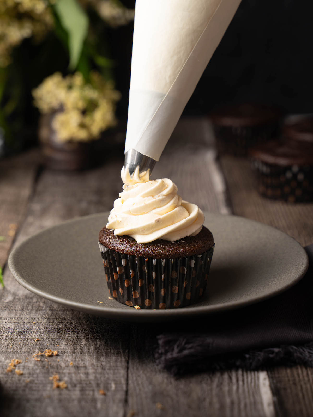 Piping elderflower buttercream frosting onto a chocolate cupcake