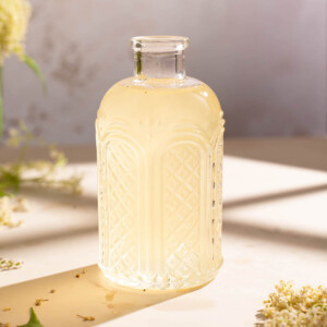 A jar of elderflower syrup sitting in the window light on a summer afternoon