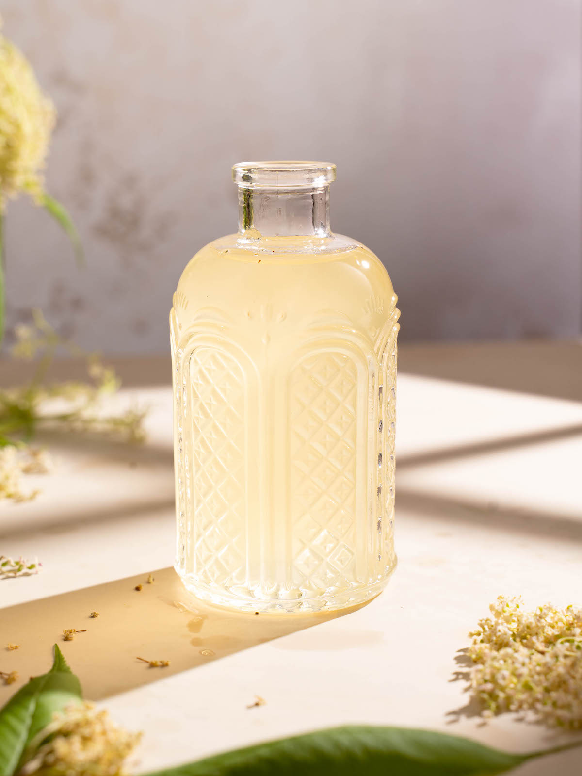 A jar of elderflower syrup sitting in the window light on a summer afternoon
