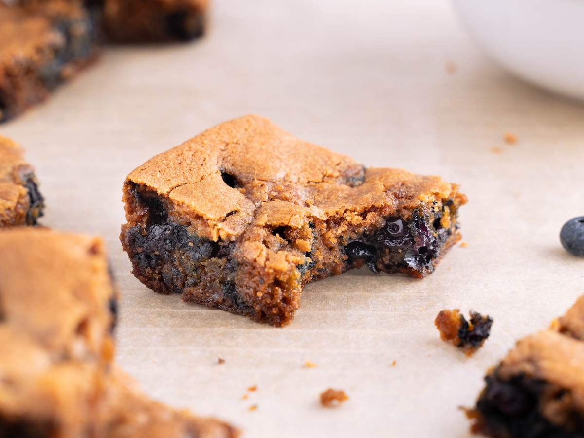 A close up look at a blueberry blondie with a bite taken out of it to show interior texture