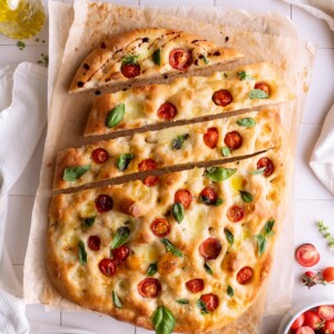 A loaf of sourdough Caprese focaccia with a few slices cut into it, drizzled with balsamic
