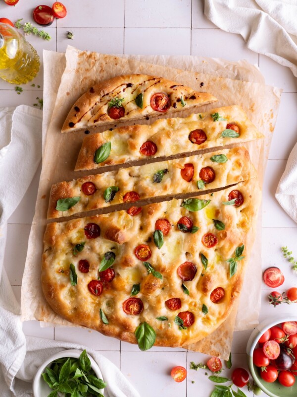 A loaf of sourdough Caprese focaccia with a few slices cut into it, drizzled with balsamic