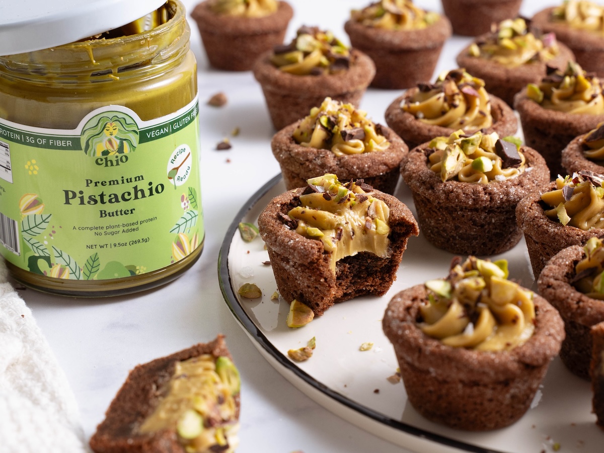 A jar of pistachio butter made by Chio, next to a platter of pistachio cookie cups