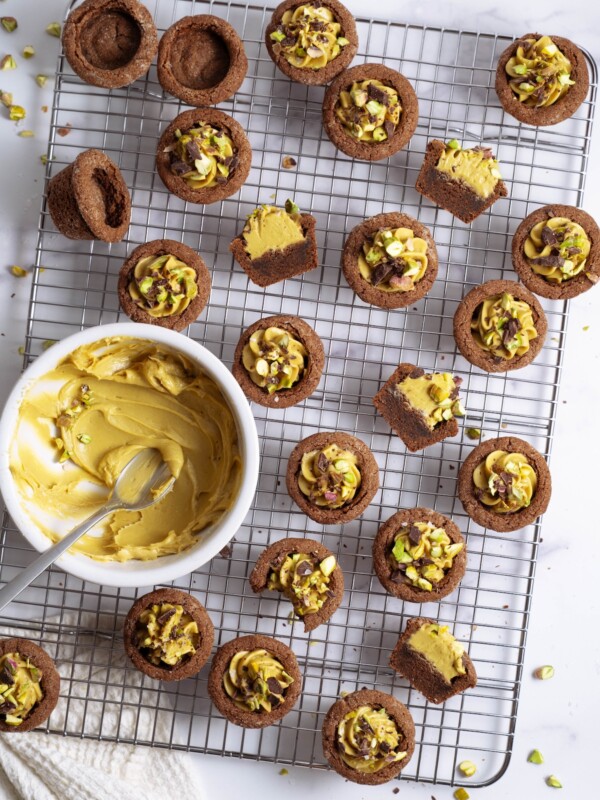 A cooling rack full of chocolate cookies filled with pistachio cream cheese frosting