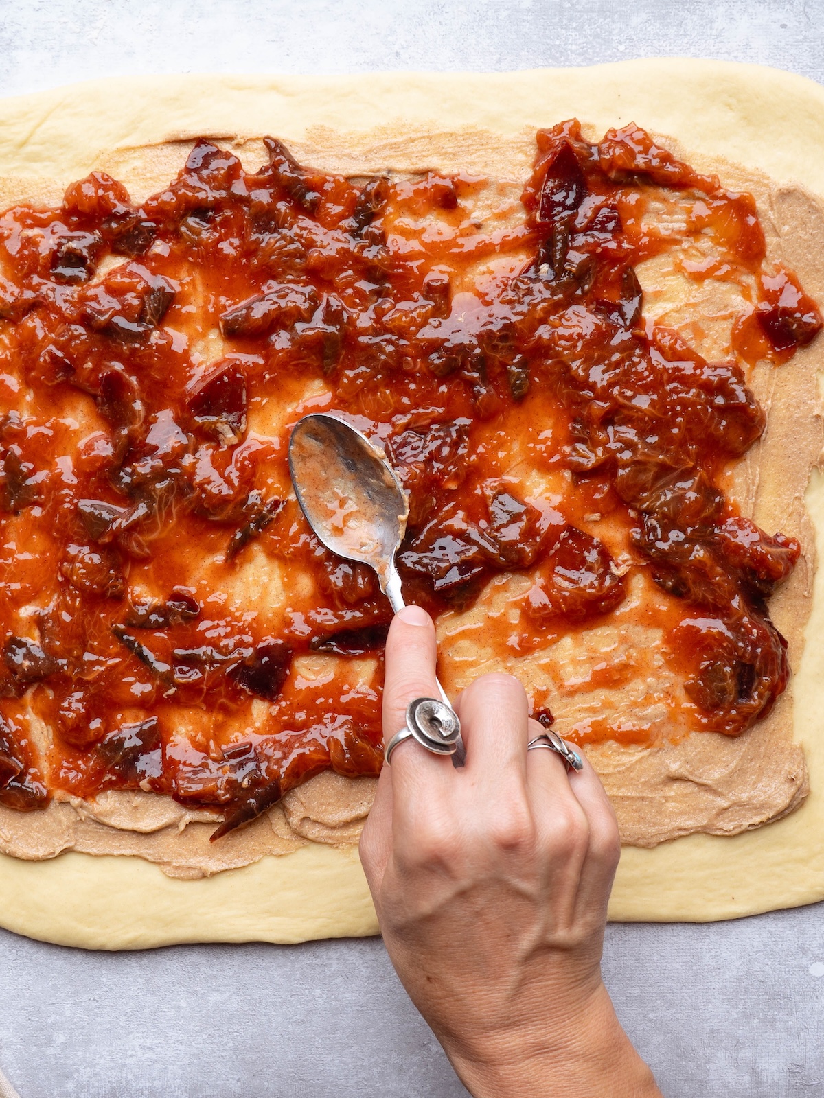 Spreading plum compote onto sweet roll dough