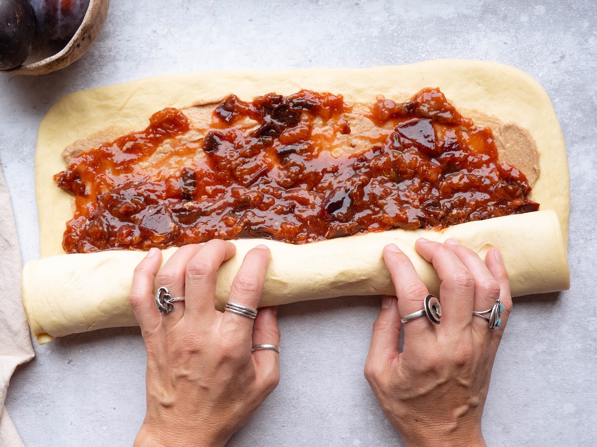 Rolling up cinnamon roll dough filled with plum compote
