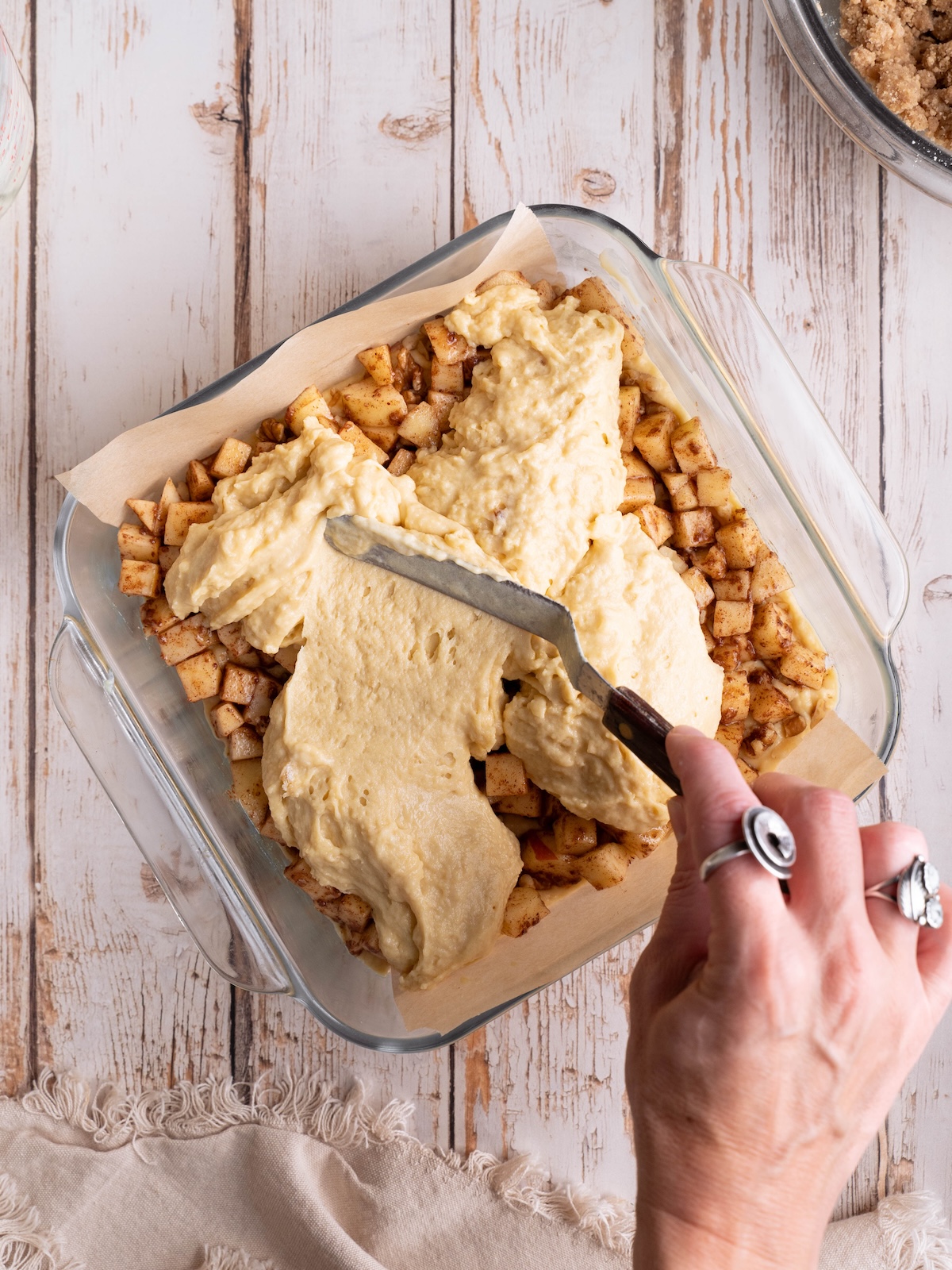 Spreading coffee cake batter over spiced apples