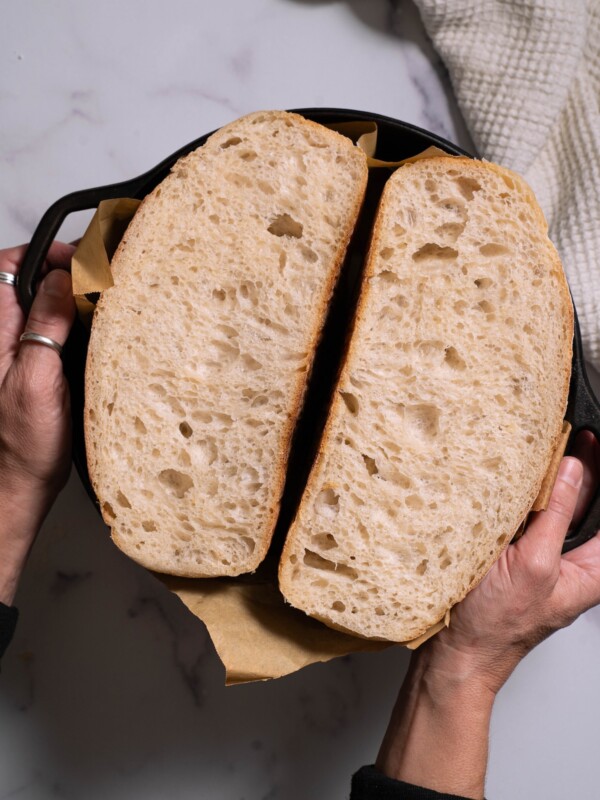 A loaf of basic sourdough bread sliced in half in a Dutch oven