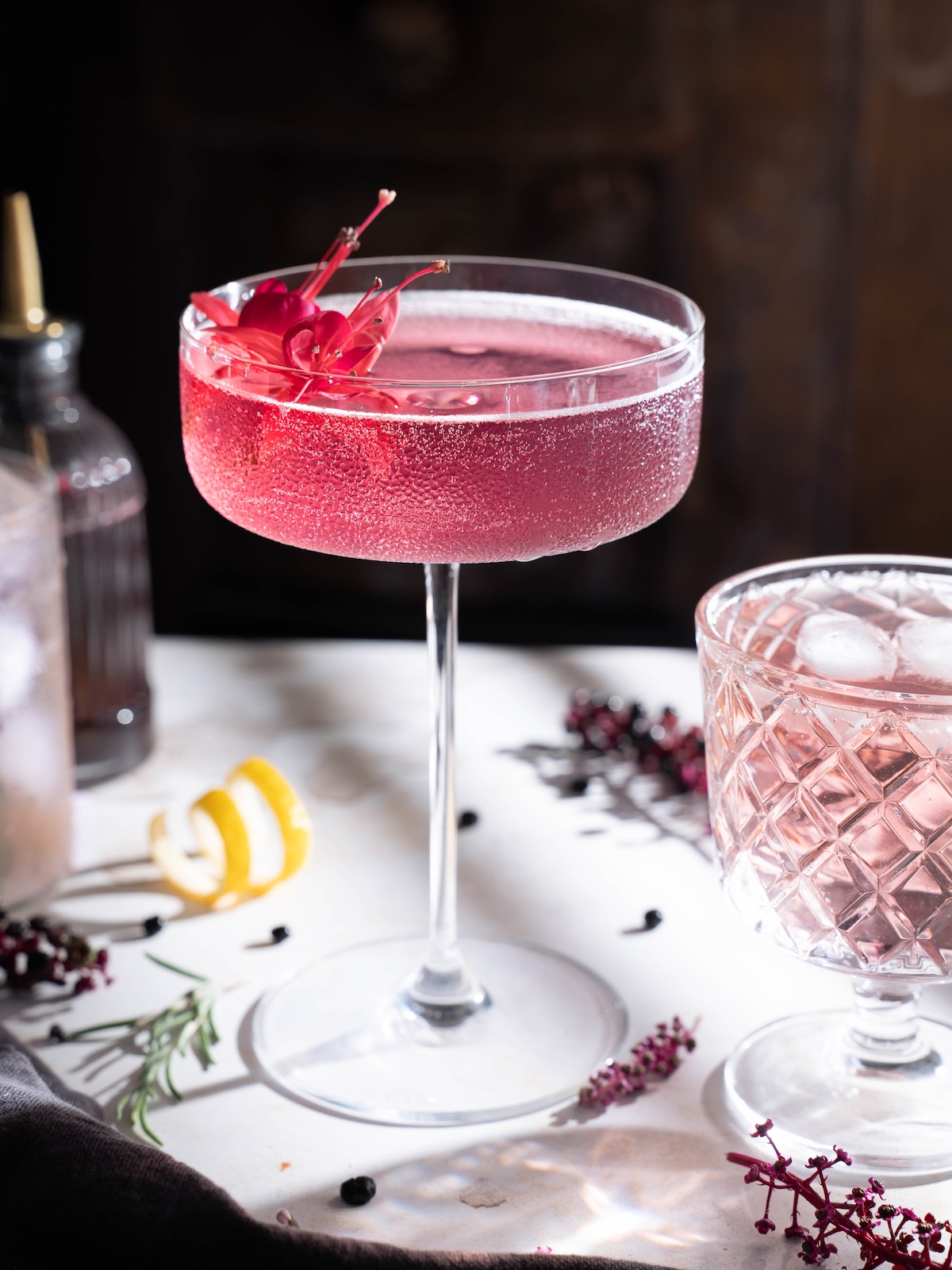 A beautifully pink elderberry cocktail served in a tall coupe glass with an edible flower garnish
