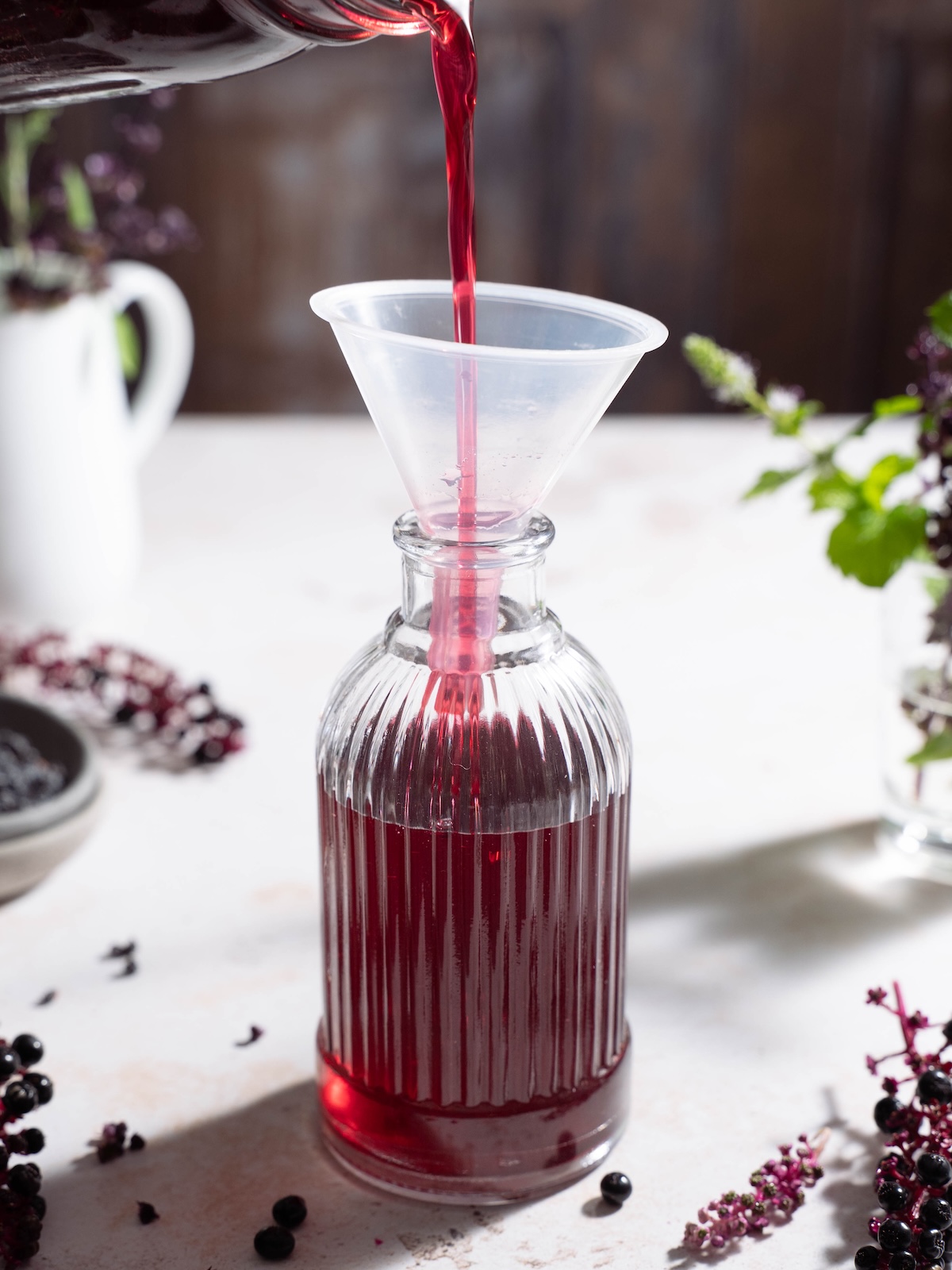 Pouring elderberry simple syrup into a glass jar