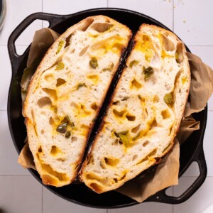 A loaf of homemade jalapeño cheddar sourdough sliced in half in a cast iron dutch oven