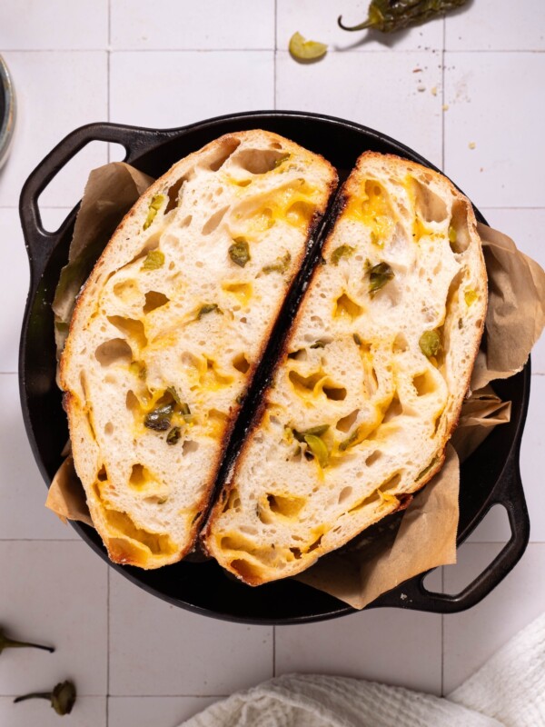 A loaf of homemade jalapeño cheddar sourdough sliced in half in a cast iron dutch oven