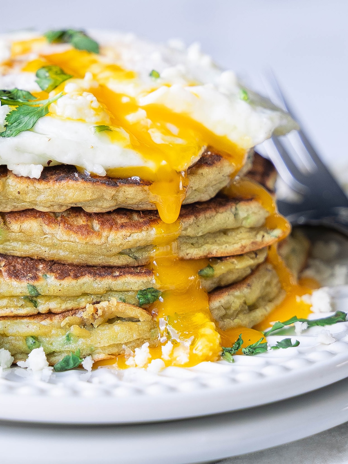 A fried egg dripping over a stack of savory pancakes