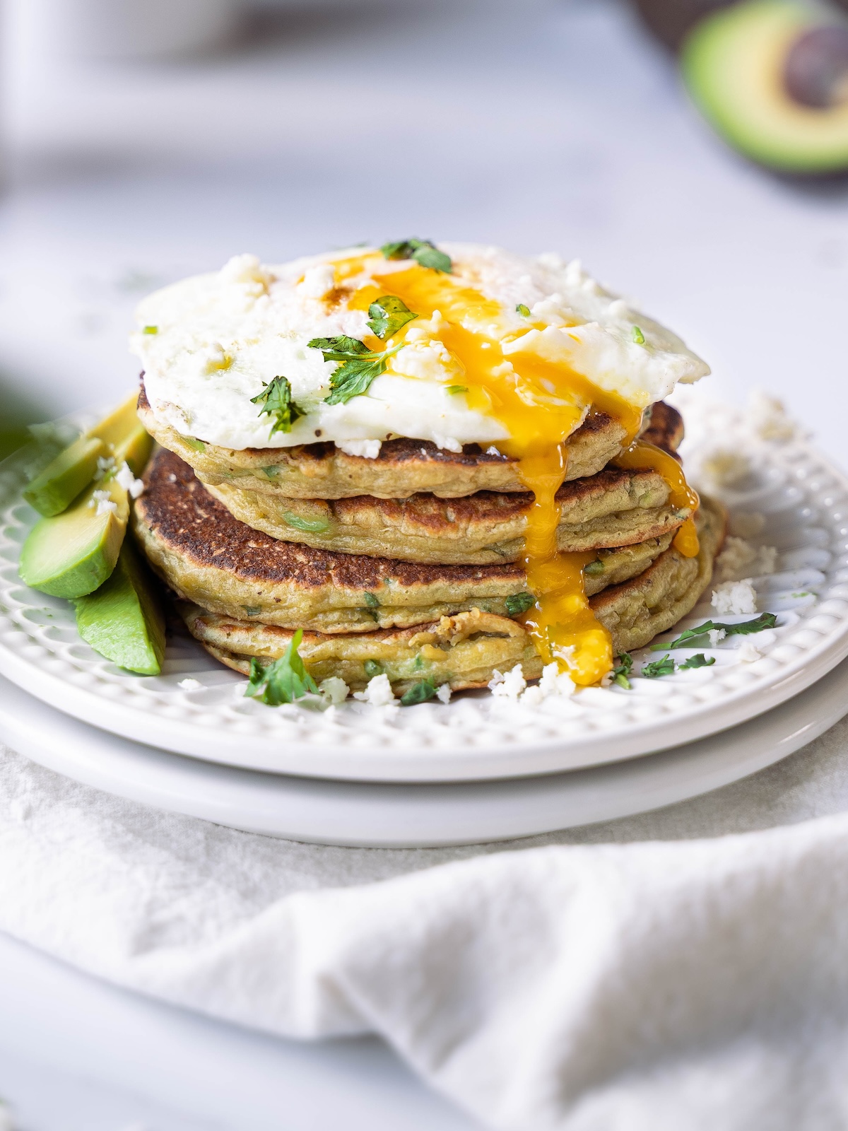 A stack of avocado pancakes with a runny fried egg on top