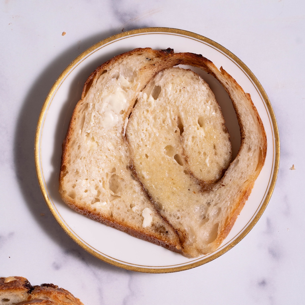 A slice of cinnamon swirl sourdough bread spread with melty butter