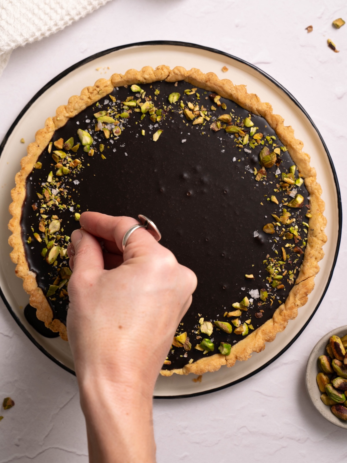 Decorating a chocolate pistachio caramel tart with pistachios and sea salt