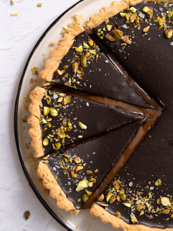 A chocolate pistachio caramel tart, sliced, with caramel oozing out between the slices