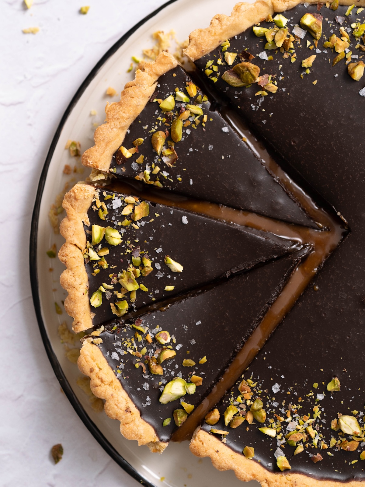 A chocolate pistachio caramel tart, sliced, with caramel oozing out between the slices