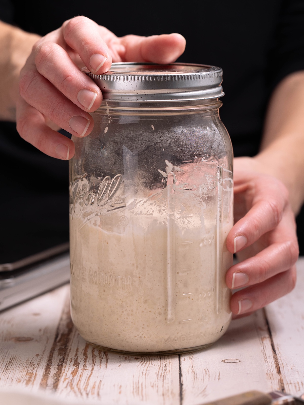 Hands holding a jar of bubbly active sourdough starter