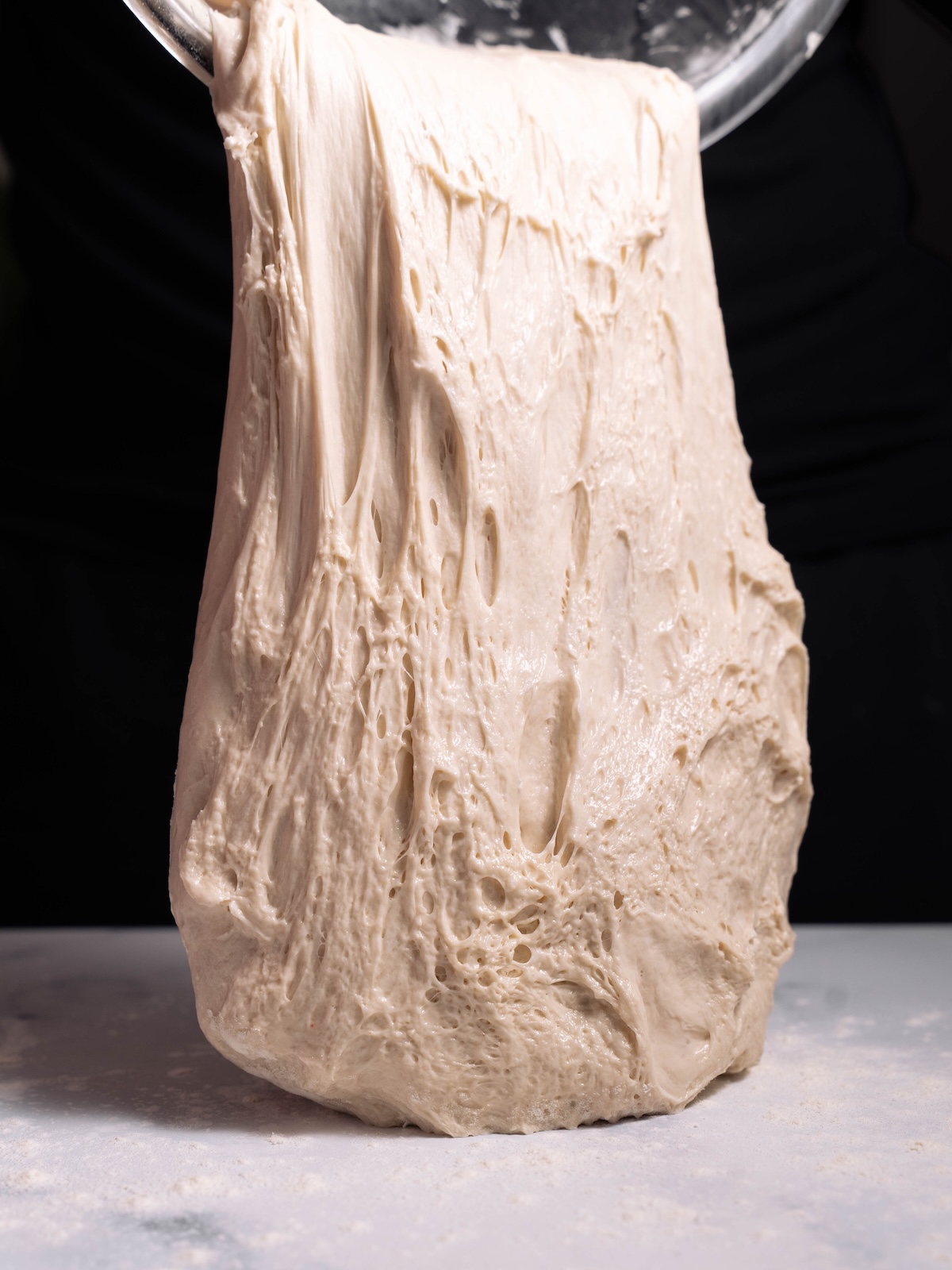 Stretchy sourdough being poured out of a mixing bowl
