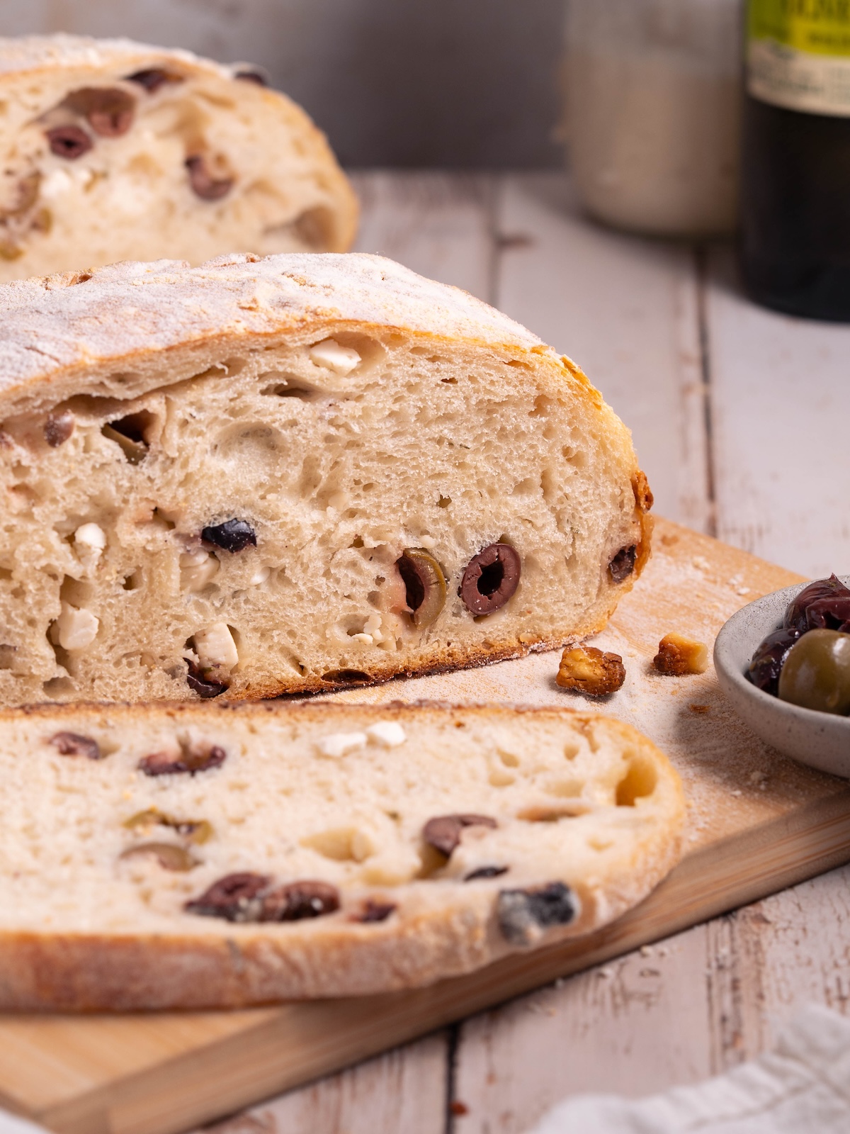 A loaf of olive sourdough sliced on a wooden board