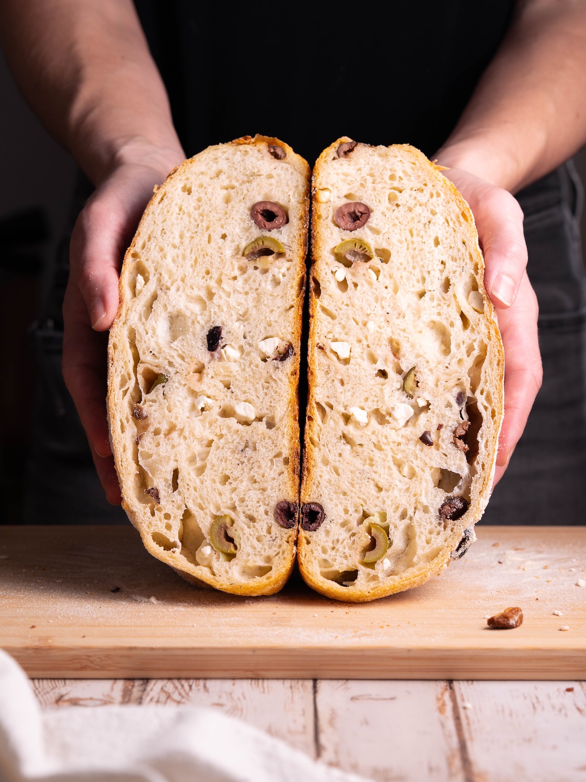 A loaf of sourdough sliced in half, showing olives and feta inside
