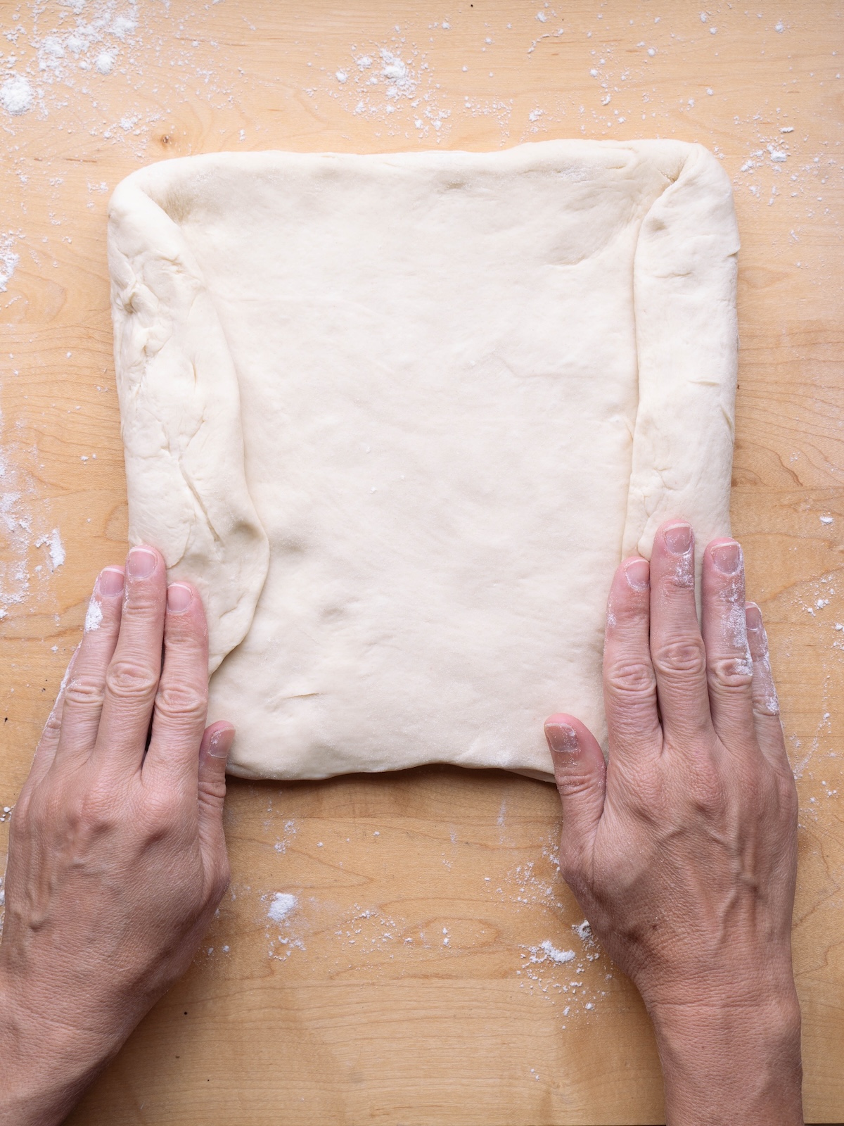 Hands folding the sides of bread dough