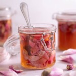 A jar of pickled magnolia petals with fresh magnolia flowers around it