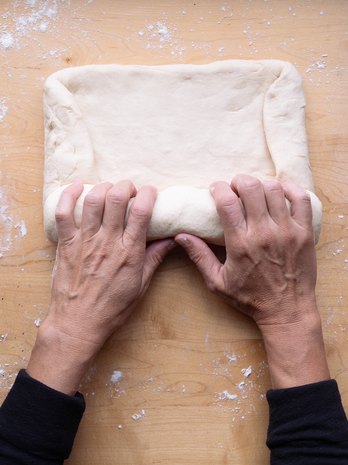 Hands rolling bread dough into a log shape