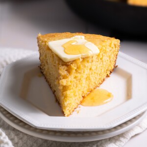 Sourdough cornbread sliced on a plate, topped with butter and honey