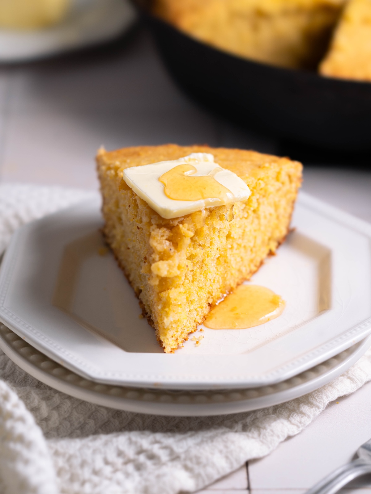 A slice of sourdough discard cornbread with butter and honey on top