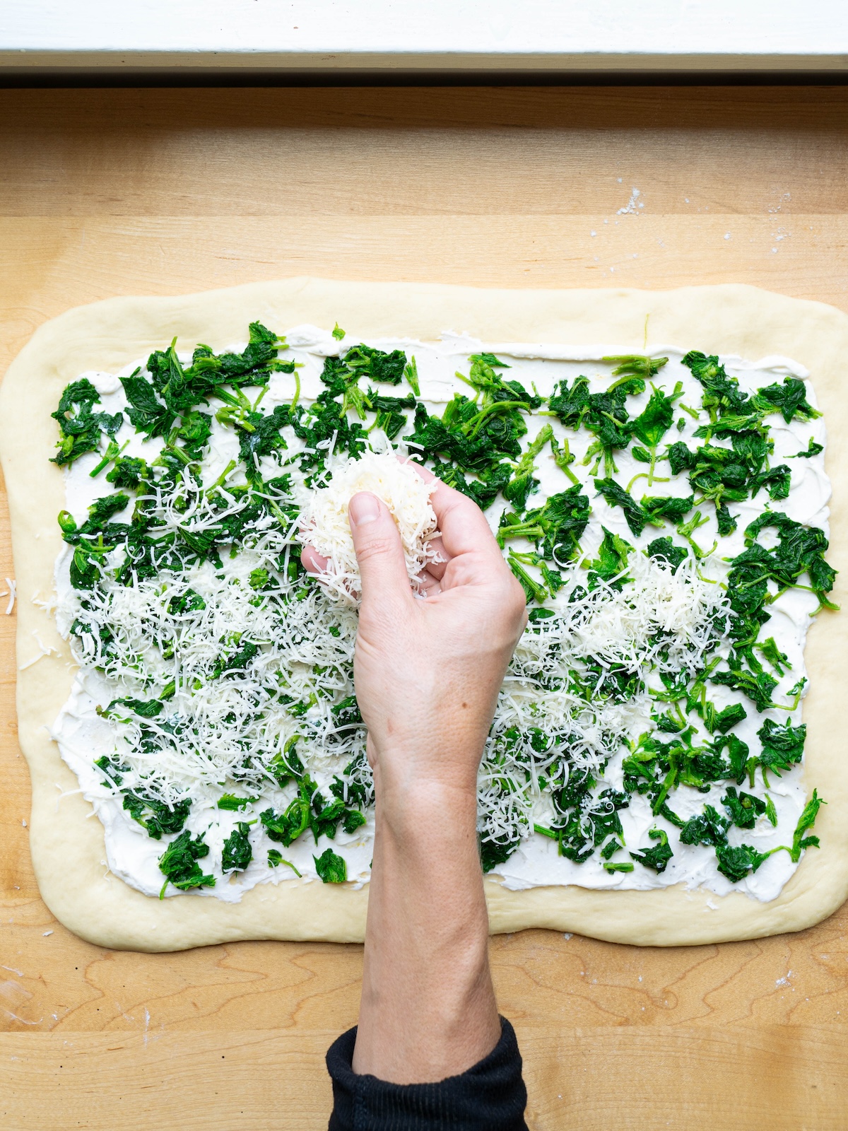 Sprinkling parmesan cheese over nettles and ricotta