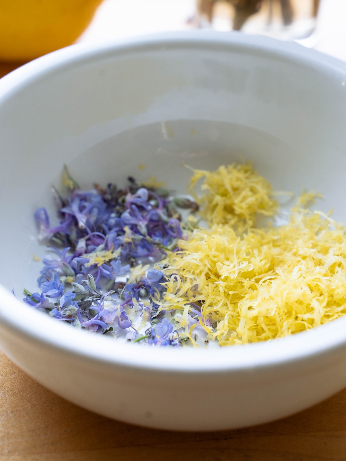 A bowl with fresh lemon zest and purple rosemary blossoms