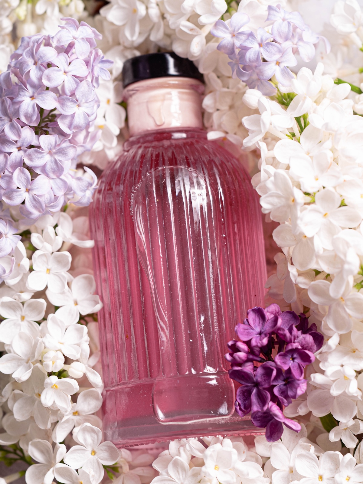 A bottle of lilac syrup surrounded by fresh lilac flowers