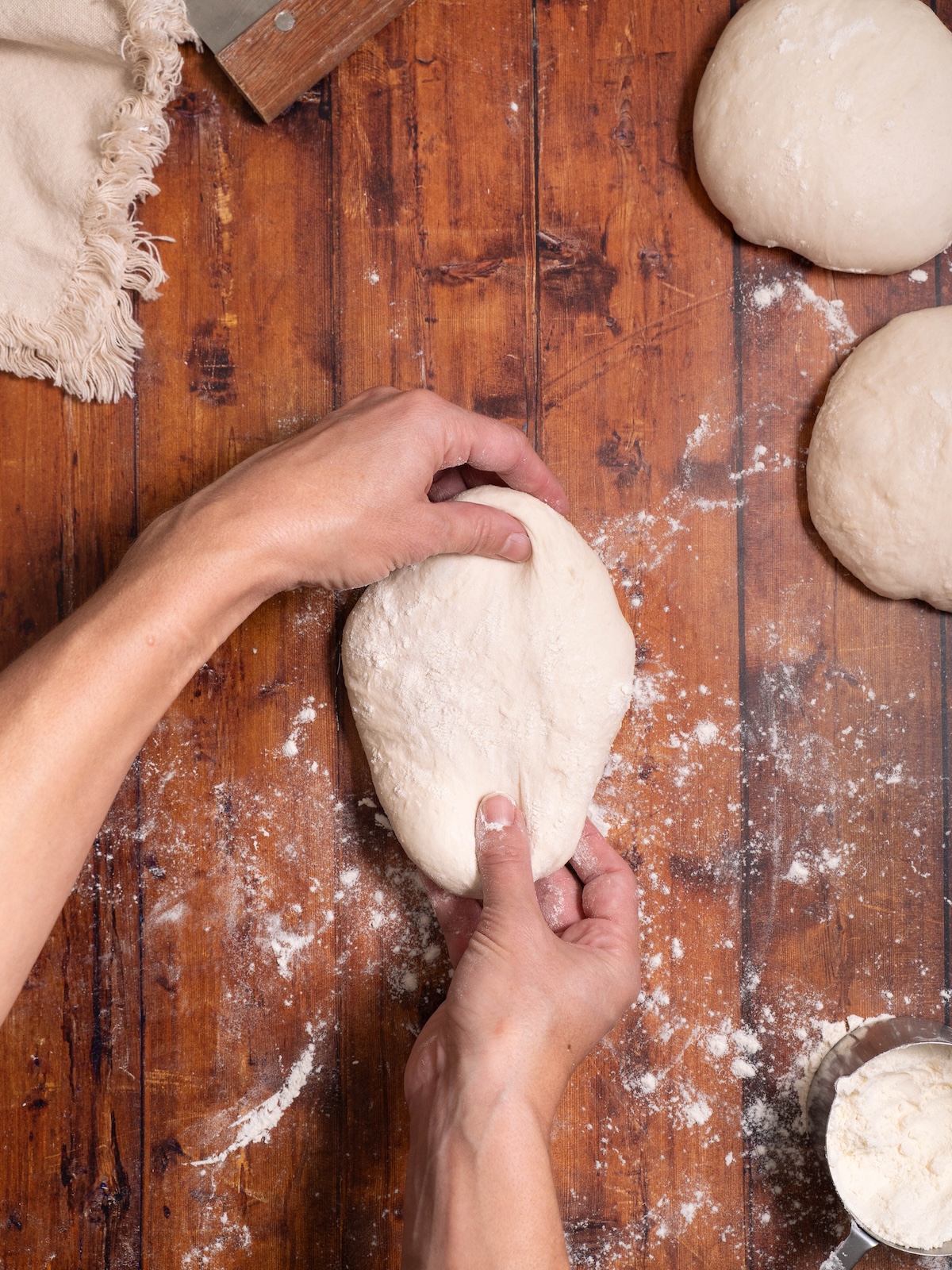 Pulling a ball of bread dough into an oval shape