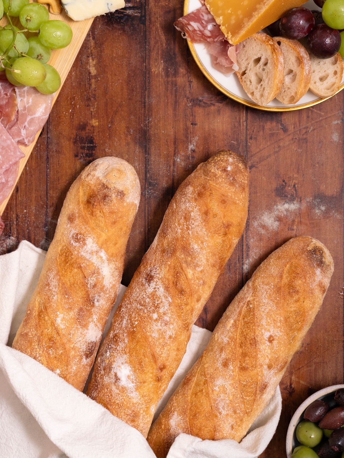 Sourdough baguettes next to a charcuterie board with meats, cheeses, and grapes
