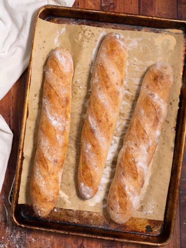 Three sourdough demi baguettes freshly baked on a baking sheet