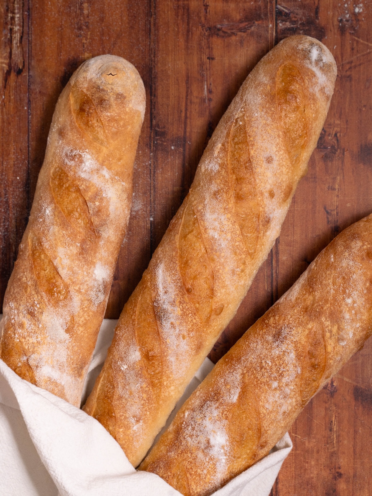 Three sourdough demi baguettes, baked and wrapped in a tea towel