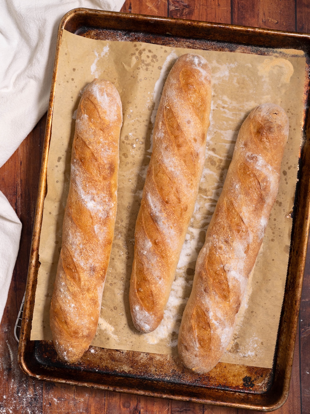 Three sourdough demi baguettes freshly baked on a baking sheet