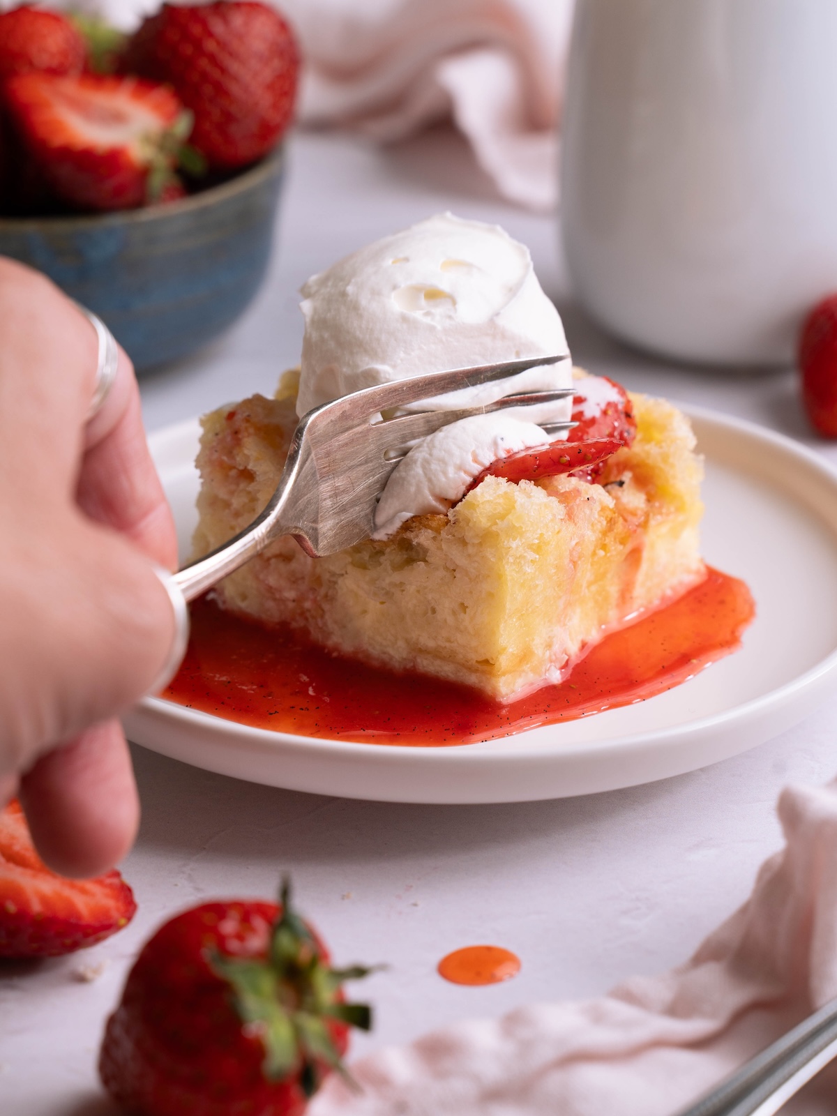 A fork sinking into sourdough bread pudding with whipped cream and strawberries