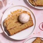Slices of rhubarb crumble cake on white plates, served with dollops of magnolia whipped cream
