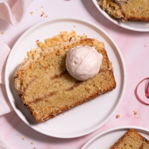 Slices of rhubarb crumble cake on white plates, served with dollops of magnolia whipped cream